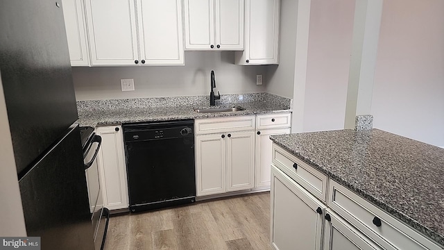 kitchen featuring light wood finished floors, white cabinets, a sink, dark stone counters, and black appliances