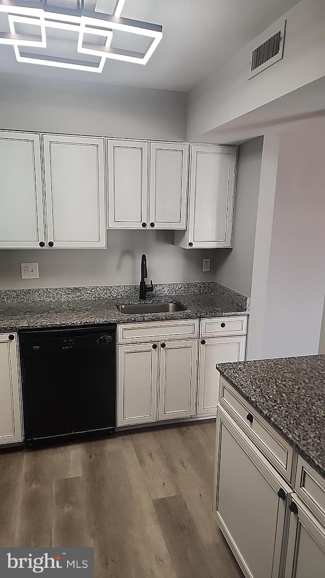 kitchen featuring wood finished floors, a sink, visible vents, dishwasher, and dark stone countertops