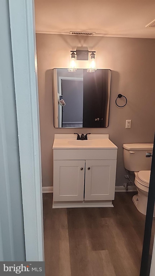 half bathroom with toilet, wood finished floors, vanity, and baseboards