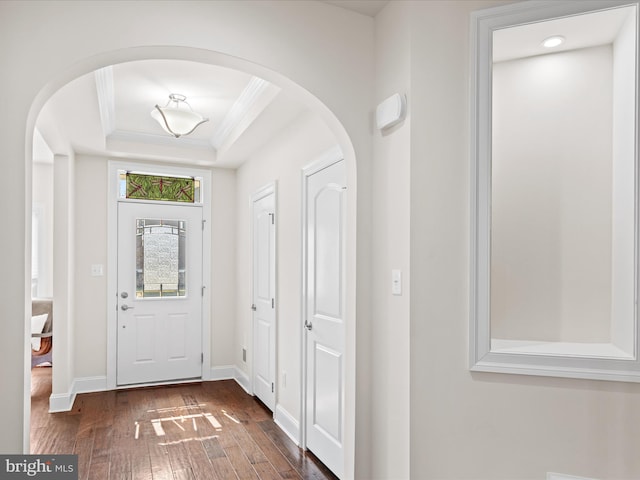 entrance foyer featuring arched walkways, baseboards, wood-type flooring, a raised ceiling, and crown molding