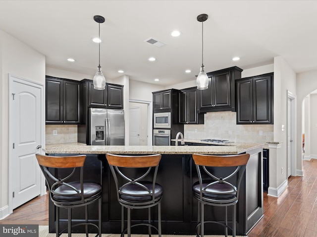 kitchen with arched walkways, visible vents, stainless steel appliances, and dark cabinetry