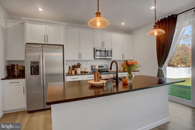 kitchen with white cabinetry, hanging light fixtures, an island with sink, and appliances with stainless steel finishes