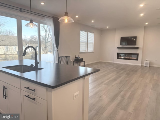 kitchen with sink, an island with sink, white cabinets, decorative light fixtures, and light wood-type flooring