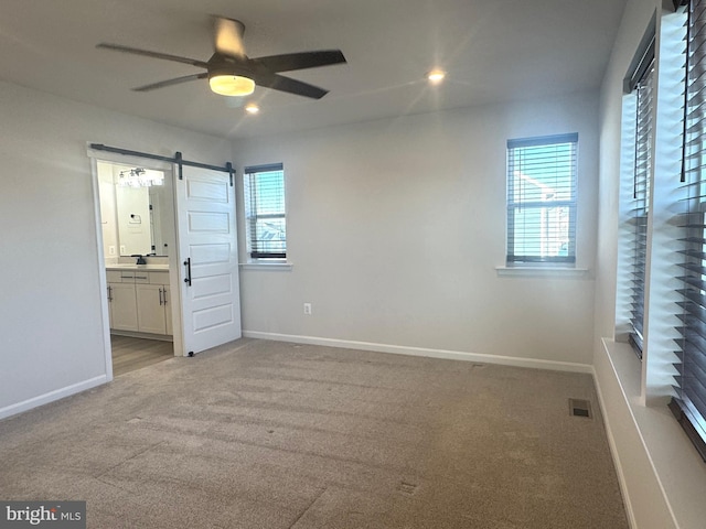 unfurnished bedroom with light colored carpet, a barn door, ceiling fan, and ensuite bathroom