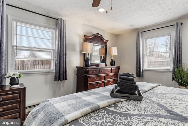 bedroom featuring multiple windows, baseboard heating, ceiling fan, and a textured ceiling