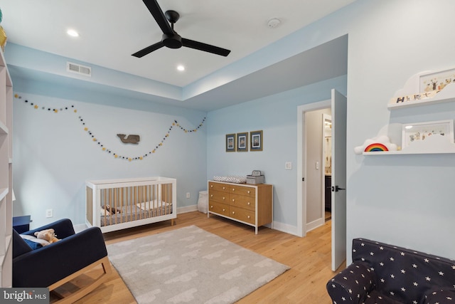 bedroom with a crib, ceiling fan, and light hardwood / wood-style floors