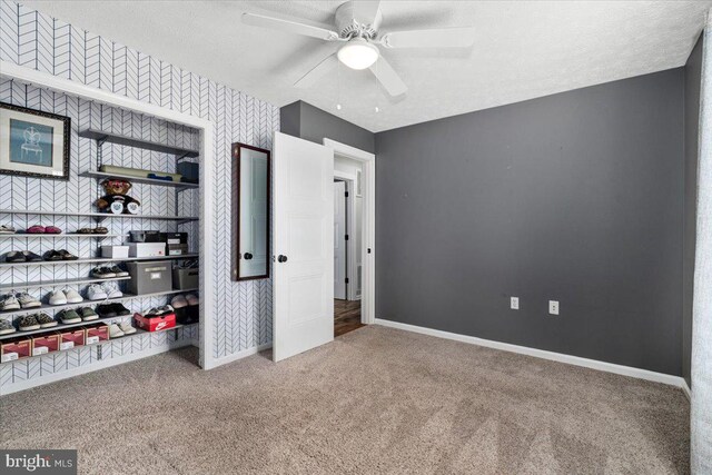 unfurnished bedroom featuring a ceiling fan, a textured ceiling, wallpapered walls, baseboards, and carpet flooring