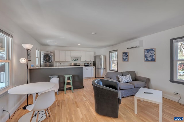 living room with stacked washer / dryer, an AC wall unit, a wealth of natural light, and light hardwood / wood-style flooring