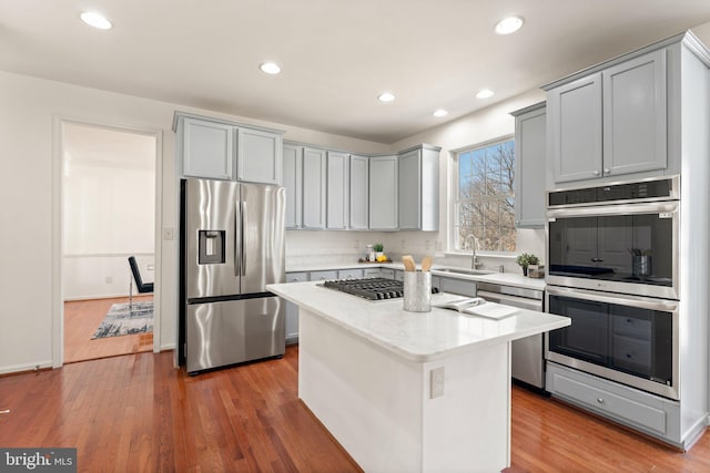 kitchen with stainless steel appliances, gray cabinets, a kitchen island, a sink, and wood finished floors