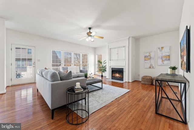 living area with baseboards, a fireplace with flush hearth, hardwood / wood-style flooring, and a ceiling fan