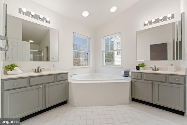 full bath featuring a bath, a shower stall, two vanities, and a sink