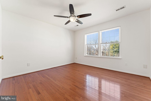 empty room featuring wood-type flooring, visible vents, and baseboards