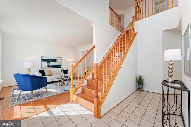 stairway with ornamental molding, tile patterned flooring, a towering ceiling, and baseboards