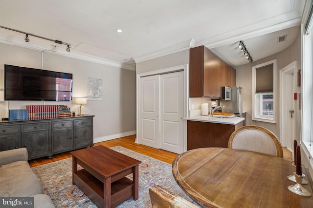 living area featuring rail lighting, visible vents, ornamental molding, light wood-type flooring, and baseboards