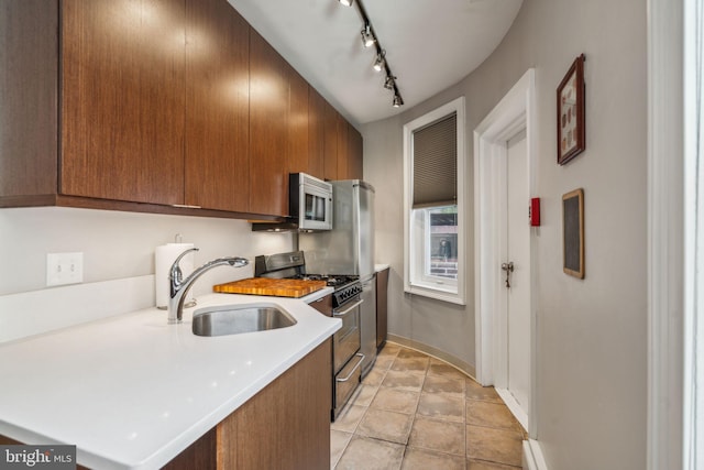 kitchen featuring a sink, light countertops, brown cabinets, stainless steel range, and rail lighting