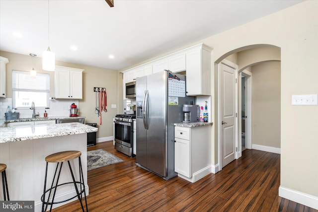 kitchen featuring a breakfast bar, light stone counters, white cabinetry, stainless steel appliances, and hanging light fixtures