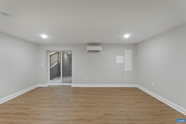 unfurnished room with electric panel, a wall unit AC, and light hardwood / wood-style floors