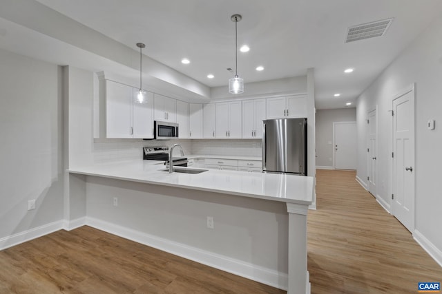 kitchen with appliances with stainless steel finishes, pendant lighting, white cabinetry, sink, and kitchen peninsula