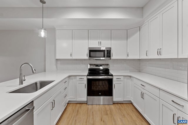 kitchen with sink, light hardwood / wood-style flooring, hanging light fixtures, stainless steel appliances, and white cabinets