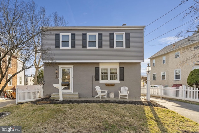 colonial inspired home featuring a front yard, fence, brick siding, and driveway