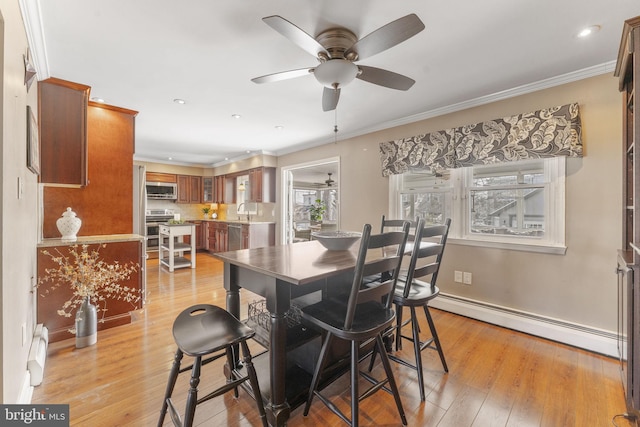 dining space featuring light wood-type flooring, a ceiling fan, crown molding, a baseboard radiator, and baseboards