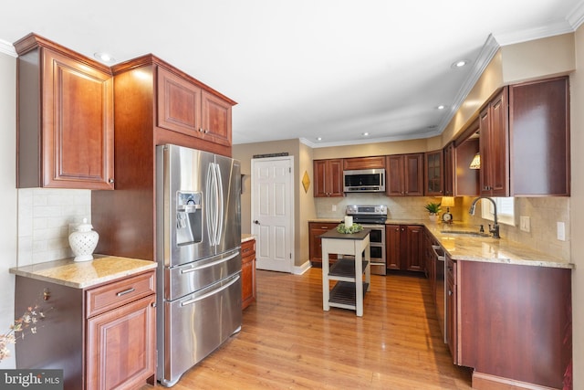 kitchen with crown molding, light stone counters, light wood-style flooring, stainless steel appliances, and a sink