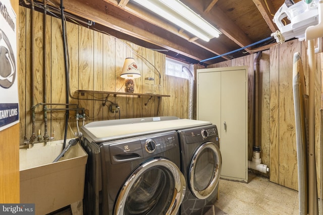 clothes washing area with wooden walls, laundry area, a sink, tile patterned floors, and washing machine and dryer