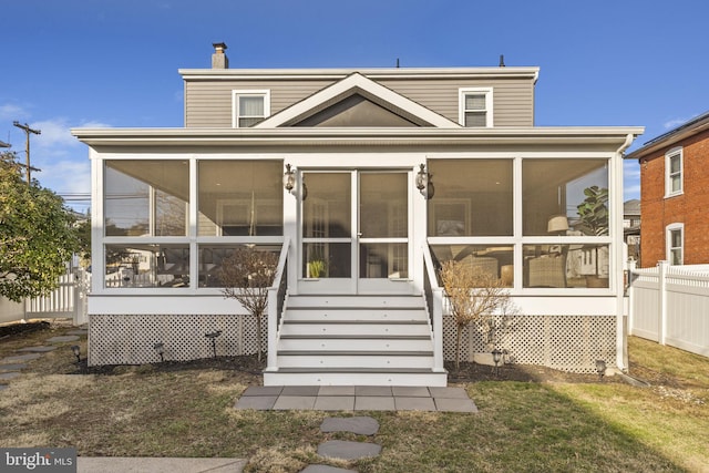 rear view of property featuring a lawn, a chimney, fence, a sunroom, and stairs