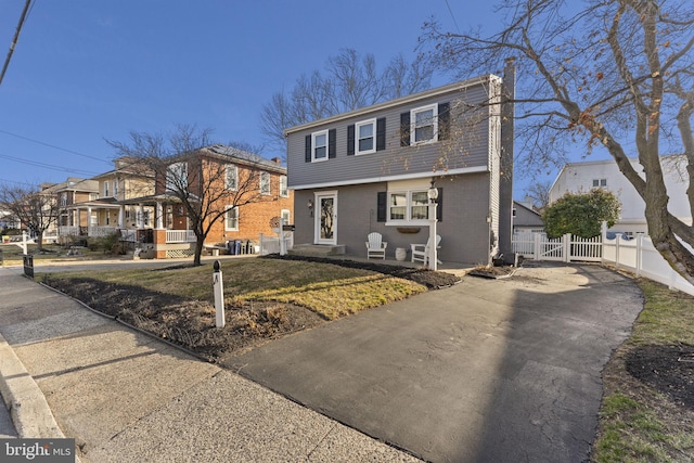 colonial inspired home featuring a gate, fence, driveway, brick siding, and a residential view