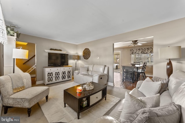 living room featuring baseboards, stairs, a ceiling fan, and wood finished floors