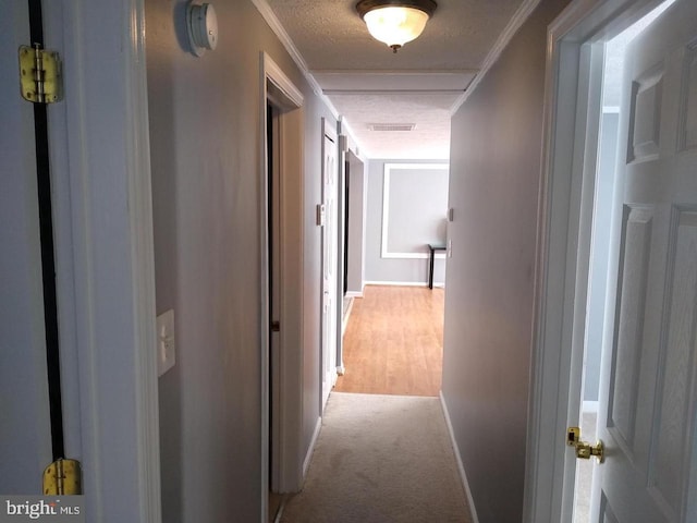 hall with ornamental molding, light colored carpet, a textured ceiling, and baseboards