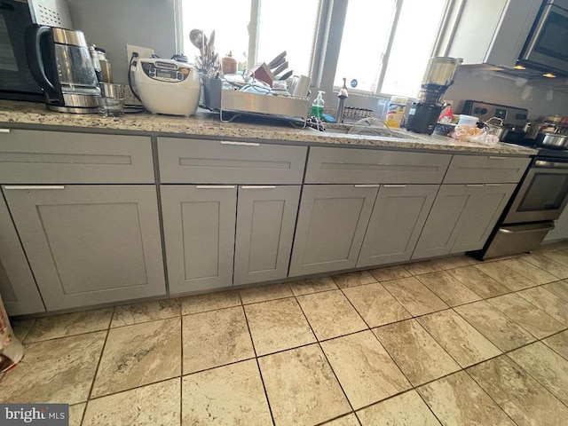 kitchen with stainless steel appliances, gray cabinets, light stone counters, and light tile patterned floors