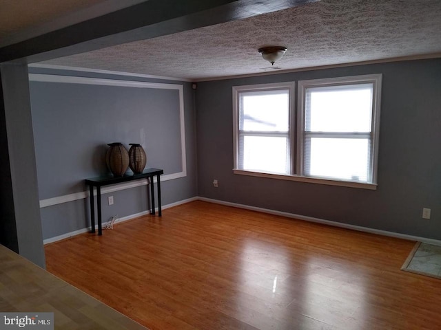 interior space featuring baseboards, a textured ceiling, ornamental molding, and wood finished floors