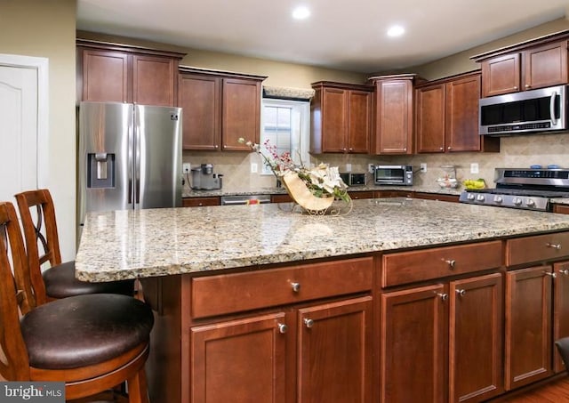 kitchen featuring a breakfast bar, a center island, decorative backsplash, appliances with stainless steel finishes, and light stone countertops