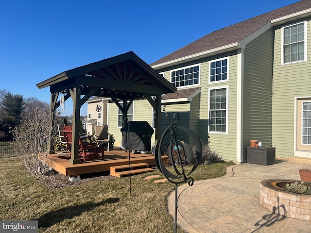 back of property with a deck, a gazebo, a fire pit, and roof with shingles