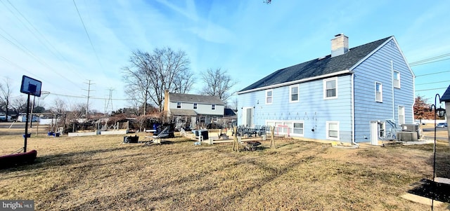 back of house featuring central AC, a lawn, and a chimney