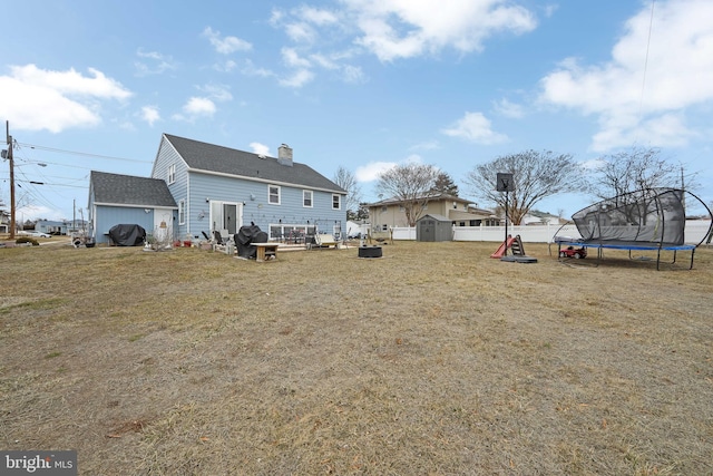 rear view of house with a trampoline, a lawn, a chimney, and fence