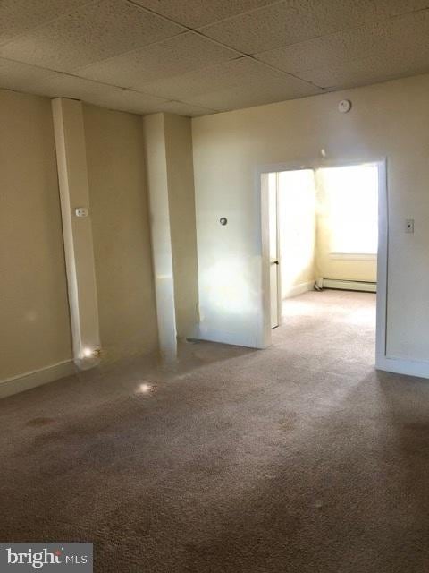 carpeted empty room with a baseboard heating unit and a paneled ceiling