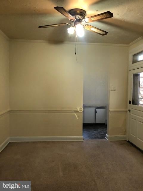 unfurnished room featuring dark carpet, crown molding, and ceiling fan