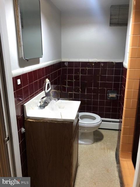 bathroom featuring toilet, baseboard heating, tile walls, and vanity