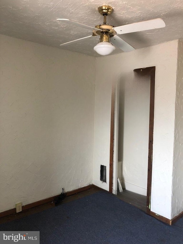 spare room featuring a textured ceiling, dark carpet, and ceiling fan