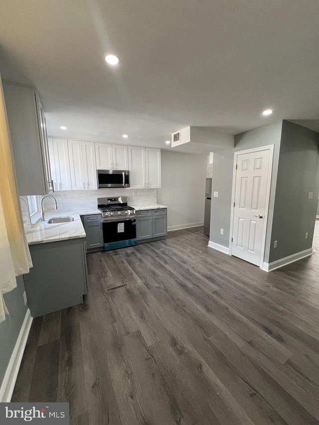 kitchen with a sink, light countertops, appliances with stainless steel finishes, dark wood finished floors, and gray cabinets