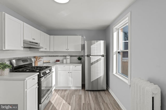 kitchen featuring white cabinetry, light wood-type flooring, appliances with stainless steel finishes, radiator, and decorative backsplash