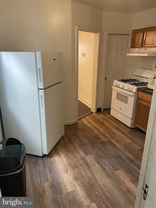 kitchen with dark wood finished floors, decorative backsplash, brown cabinetry, white appliances, and under cabinet range hood