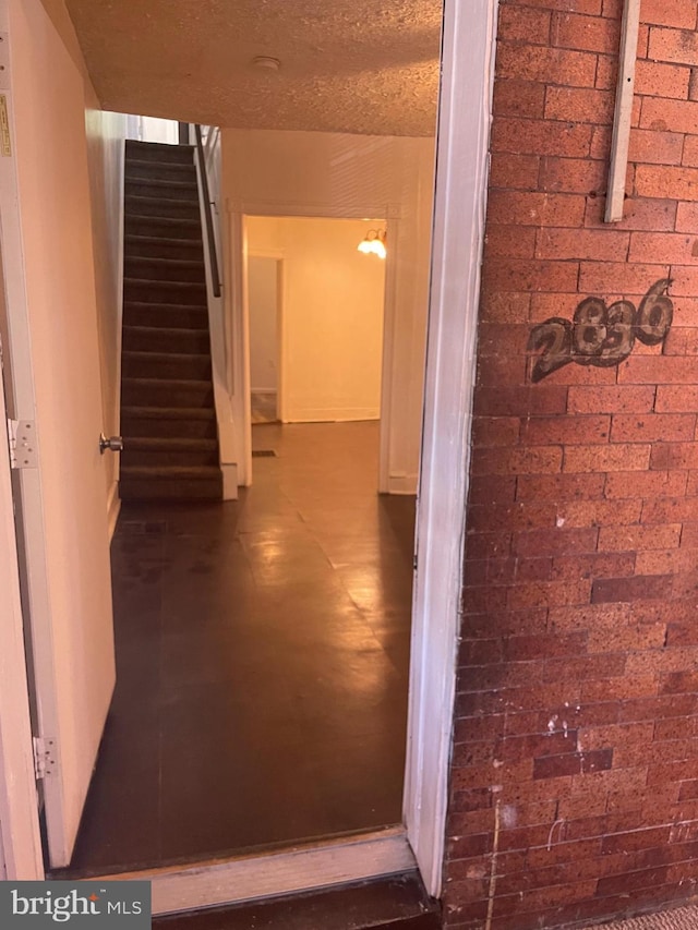 hallway with brick wall, stairway, and a textured ceiling