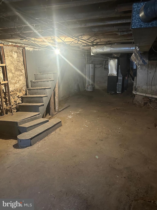 unfinished below grade area featuring water heater, heating unit, and stairs