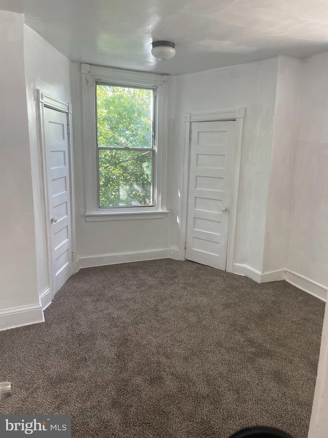 empty room with baseboards and dark colored carpet