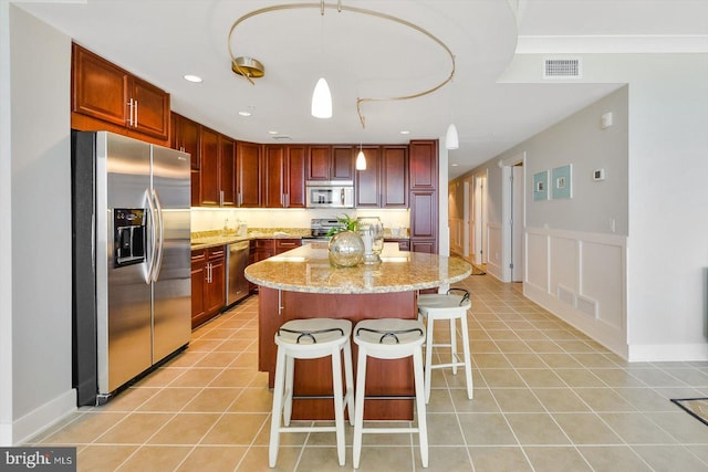 kitchen with light tile patterned flooring, a kitchen island, decorative light fixtures, stainless steel appliances, and light stone countertops