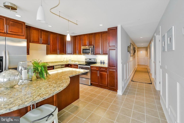 kitchen with appliances with stainless steel finishes, hanging light fixtures, a breakfast bar area, light stone countertops, and light tile patterned flooring