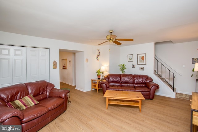 living room with light wood finished floors, stairs, baseboards, and a ceiling fan